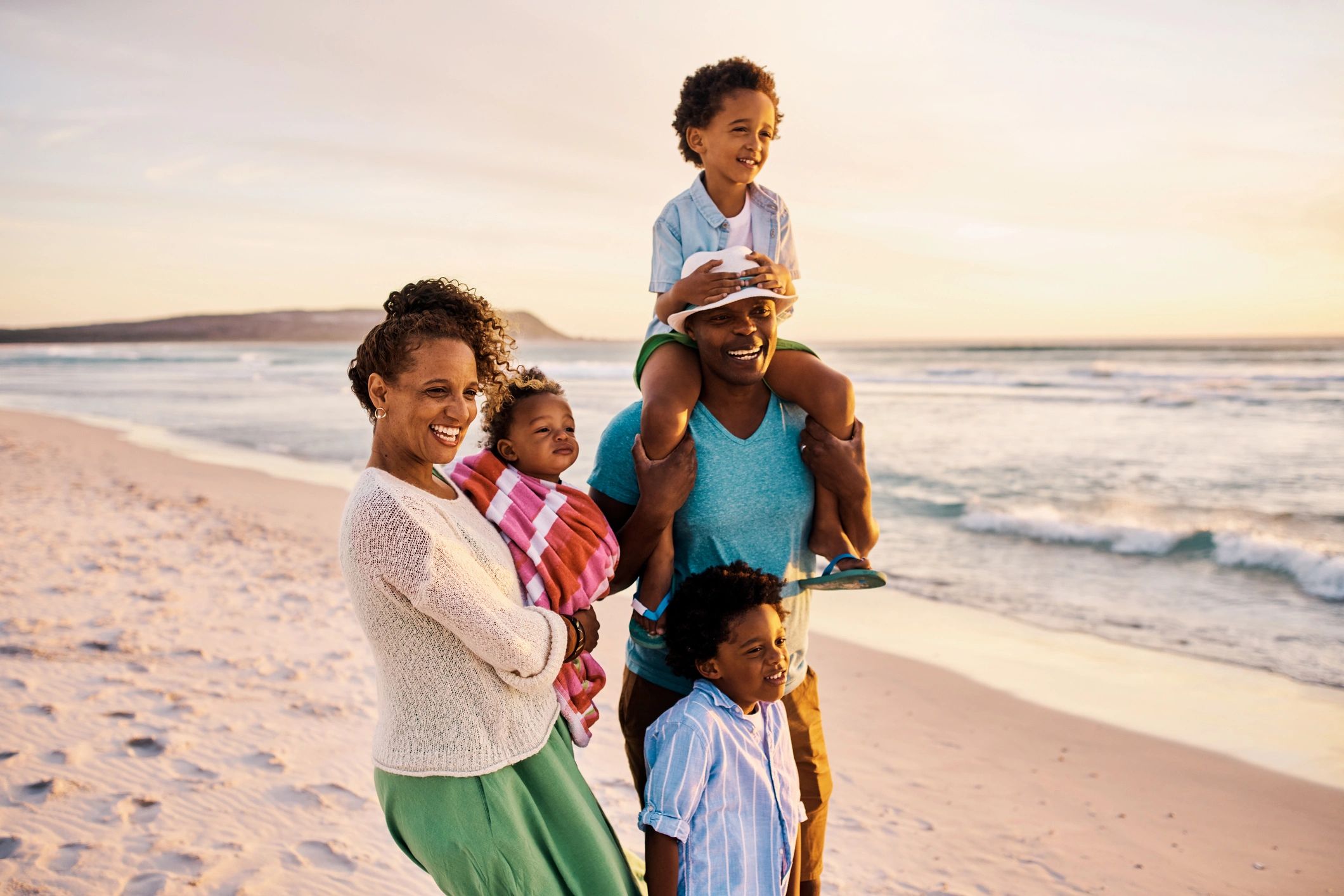 Young family relaxing on the beach together on the weekend. Parents looking at the view on the seashore with their children during a getaway vacation. Boys bonding with their mom and dad on holiday